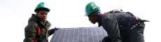 Two volunteers on a roof installing a solar panel.